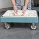 A person in gloves using a Cambro pizza dough box dollie to hold dough on a tray.