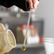 A person using a Vollrath stainless steel long handled measuring spoon to measure liquid.