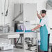 A man wearing a blue apron using a Noble Warewashing door type dishwasher.