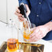 A person using an iSi Stainless Steel Soda Siphon to pour a drink into a glass.