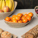 A 10 Strawberry Street Tiger Eye porcelain canoe bowl filled with oranges and bananas on a table with other bowls of fruit and cookies.