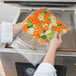 A person holding a VacPak-It 12" x 16" vacuum packaging bag of vegetables.