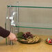 A person using an Advance Tabco food shield to cover a buffet of cookies, fruit, and chocolate-covered strawberries.