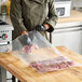 A person's arm holding a VacPak-It plastic bag with raw meat.