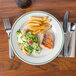 A Homer Laughlin ivory china plate with salmon, fries, and salad on it, with a fork next to it.