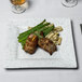 A 10 Strawberry Street blue speckled porcelain dinner plate with meat and asparagus on it on a table.