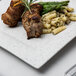 A 10 Strawberry Street blue speckled square porcelain dinner plate with meat and asparagus on it.