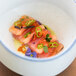 A white 10 Strawberry Street Arctic Blue porcelain bowl with food, flowers, and herbs.