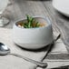 An Arctic Blue porcelain demi bowl of soup with parsley on a napkin and a spoon.