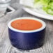 A Tuxton cobalt and eggshell white china ramekin filled with sauce on a wood table.