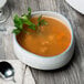 A white porcelain cereal bowl filled with soup on a table with a spoon.