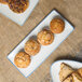 A 10 Strawberry Street Arctic Blue rectangular porcelain platter holding a variety of pastries on a table in a bakery display.