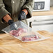 A person in gloves cutting meat in a VacPak-It plastic bag.