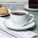 A white 10 Strawberry Street porcelain cup filled with brown liquid and pastries on a plate.