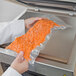 A person's hand holding a VacPak-It chamber vacuum packaging bag filled with carrots.