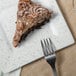 A piece of chocolate cake with frosting and pecans on a 10 Strawberry Street blue speckled porcelain square plate with a fork.