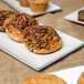 A rectangular porcelain platter with a cinnamon roll and pastries with nuts and seeds.