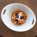 A blue speckled porcelain bowl with cut-out handles holding pasta with basil and cheese.