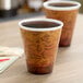 Two Dart Fusion Escape foam cups with a world map design on a table full of coffee.