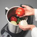 A person holding a tomato and onion in a bowl.