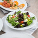 A Tuxton Charleston white china bowl filled with salad on a table.