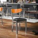 A metal chair with a black vinyl seat and a cherry wood backrest.