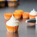 A cupcake in an Ateco orange striped baking cup on a table.