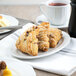 A Tuxton Charleston bright white china oval platter with scones, butter, and coffee on it.