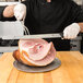 A chef using a Victorinox slicing knife to cut ham on a cutting board.