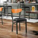 A black metal chair with a black vinyl seat and a curved cherry wood backrest.