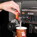 A person using a Bunn airpot coffee brewer to pour a cup of coffee.