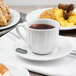 A Tuxton Charleston bright white china saucer with food and a cup of tea on it.