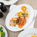 A close up of a TuxTrendz Charleston white china oval platter with shrimp and vegetables on it.