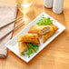 A rectangular white porcelain platter with fried spring rolls and chopsticks.