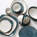 A stack of Tuxton TuxTrendz Artisan Geode Agave bread and butter plates with a white bowl with brown specks in the background.