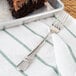 A Oneida stainless steel dessert fork on a napkin next to a slice of chocolate cake.