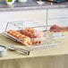 A person using a Cambro Clear Dome Display Cover with Hinged Lid to cover a tray of pastries on a counter.