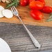 An Oneida Astragal stainless steel cocktail fork on a wooden cutting board.