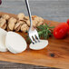 An Oneida Astragal stainless steel cocktail fork on a wooden cutting board with cheese and tomatoes.