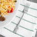 A Oneida Astragal stainless steel dinner fork on a table with a plate of noodles and meat.