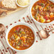 Two bowls of Spring Glen Fresh Foods vegetable soup with beef on a table with spoons and bread.