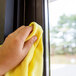 A hand using a yellow Unger SmartColor microfiber cloth to clean a window.