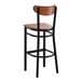 A bar stool with a black metal frame and antique walnut wood seat and back.