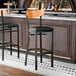 A black bar stool with a black vinyl seat and a cherry wood backrest.