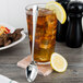 An 1880 Hospitality stainless steel iced tea spoon next to a glass of iced tea with a lemon.