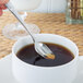 A hand holding a Oneida Astragal stainless steel demitasse spoon over a cup of coffee.