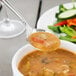 A Oneida stainless steel rounded bowl soup spoon over a bowl of soup.