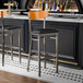 A Lancaster Table & Seating bar stool with a black cushion and cherry wood back on a counter.