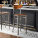 A bar stool with a clear coat metal frame and antique walnut wood seat and back.