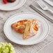 A WNA Comet white plastic plate with silver accents holding pastries with a fork.
